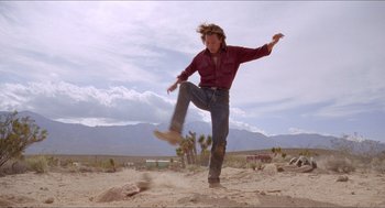 Movie still from “Tremors” (1990), directed by Ron Underwood – A man in a red shirt is kicking around in the dirt; Wide shot, Low angle