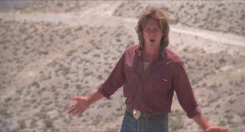 Movie still from “Tremors” (1990), directed by Ron Underwood – A man in a red shirt is standing in the desert; Medium shot, Low angle