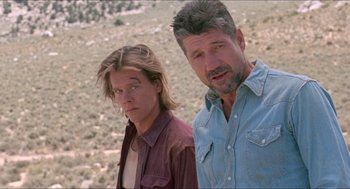 Movie still from “Tremors” (1990), directed by Ron Underwood – A man standing next to a young man in a field; Close Up shot, Low angle