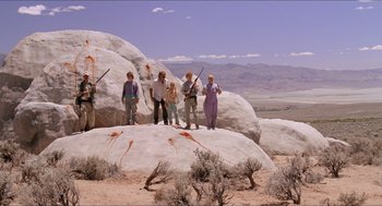 Movie still from “Tremors” (1990), directed by Ron Underwood – A group of people standing on top of a large rock; Wide shot, Low angle