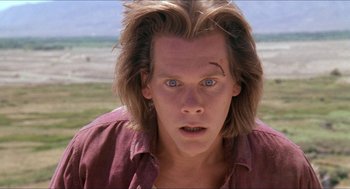 Movie still from “Tremors” (1990), directed by Ron Underwood – A man with long blonde hair and blue eyes stares at the camera; Close Up shot, Low angle