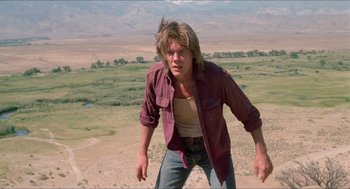 Movie still from “Tremors” (1990), directed by Ron Underwood – A man standing on top of a grass covered field; Medium shot, Low angle