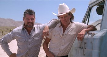 Movie still from “Tremors” (1990), directed by Ron Underwood – A man in a white cowboy hat is leaning on another man; Medium shot, Low angle