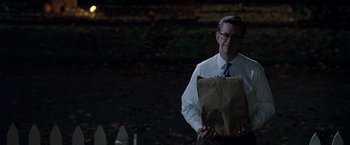 Movie still from “Trick 'r Treat” (2007), directed by Michael Dougherty – A man holding a paper bag while standing in a dark room; Medium shot, Over the shoulder angle