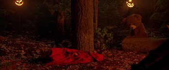 Movie still from “Trick 'r Treat” (2007), directed by Michael Dougherty – A person is laying on the ground near a tree in the woods; Extreme Wide shot, Overhead angle