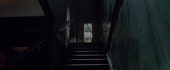 Movie still from “Trick 'r Treat” (2007), directed by Michael Dougherty – A dark room with a staircase leading up to a window; Wide shot, Low angle