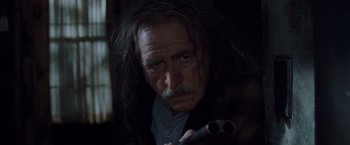 Movie still from “Trick 'r Treat” (2007), directed by Michael Dougherty – An old man with long grey hair holding a gun in a dark room; Close Up shot, Low angle