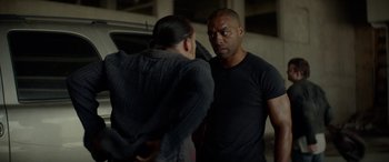 Movie still from “Triple 9” (2016), directed by John Hillcoat – A man and a woman standing next to each other in a garage; Medium shot, Over the shoulder angle