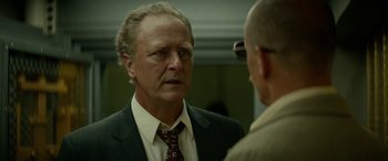 Movie still from “Triple 9” (2016), directed by John Hillcoat – A man wearing a suit and tie talking to another man in front of a mirror; Close Up shot, Over the shoulder angle