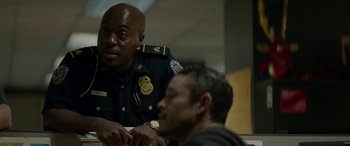 Movie still from “Triple 9” (2016), directed by John Hillcoat – A police officer sitting next to a man in front of a table; Medium shot, Over the shoulder angle
