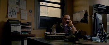 Movie still from “Triple 9” (2016), directed by John Hillcoat – A man sitting at a desk talking on the phone; Medium shot, Low angle