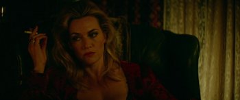 Movie still from “Triple 9” (2016), directed by John Hillcoat – A woman sitting in a chair looking at the camera; Close Up shot, Over the shoulder angle