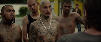 Movie still from “Triple 9” (2016), directed by John Hillcoat – A group of tattooed men standing next to each other; Medium shot, Over the shoulder angle