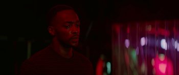 Movie still from “Triple 9” (2016), directed by John Hillcoat – A man in a striped shirt is standing in a dark room; Close Up shot, Over the shoulder angle