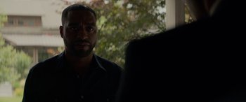 Movie still from “Triple 9” (2016), directed by John Hillcoat – A man standing in front of a tree looking at the camera; Close Up shot, Over the shoulder angle