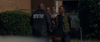 Movie still from “Triple 9” (2016), directed by John Hillcoat – A group of men standing next to each other on a field; Medium shot, Over the shoulder angle