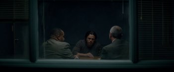 Movie still from “Triple 9” (2016), directed by John Hillcoat – A man sitting at a table with two other men; Medium shot, Over the shoulder angle