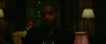 Movie still from “Triple 9” (2016), directed by John Hillcoat – A man in a black shirt holding a glass of wine; Close Up shot, Over the shoulder angle