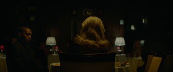 Movie still from “Triple 9” (2016), directed by John Hillcoat – A woman with long blonde hair sitting in a chair; Medium shot, Over the shoulder angle
