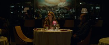 Movie still from “Triple 9” (2016), directed by John Hillcoat – A woman sitting at a table with a pink lamp; Medium shot, Low angle