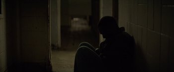 Movie still from “Triple 9” (2016), directed by John Hillcoat – A man sitting in a chair in a dark room; Medium shot, High angle