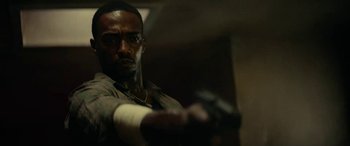 Movie still from “Triple 9” (2016), directed by John Hillcoat – A man is holding a gun in a room; Close Up shot, Low angle