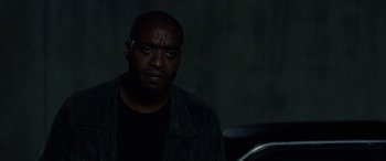 Movie still from “Triple 9” (2016), directed by John Hillcoat – A man sitting in front of a chair in a dark room; Close Up shot, Low angle