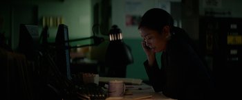 Movie still from “Triple 9” (2016), directed by John Hillcoat – A woman sitting at a table talking on a phone; Medium shot, High angle