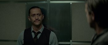 Movie still from “Triple 9” (2016), directed by John Hillcoat – A man in a vest and tie standing in front of a wall; Close Up shot, Low angle