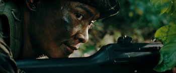 Movie still from “Triple Threat” (2019), directed by Jesse V. Johnson – A man in a camouflage hat is holding a rifle; Extreme Close Up shot, Over the shoulder angle