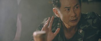 Movie still from “Triple Threat” (2019), directed by Jesse V. Johnson – A person holding a towel over their ear; Close Up shot, Over the shoulder angle