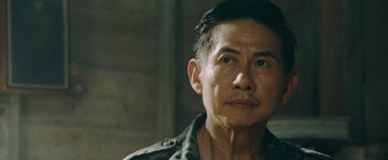 Movie still from “Triple Threat” (2019), directed by Jesse V. Johnson – An older asian man looking at the camera; Close Up shot, Over the shoulder angle