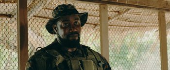 Movie still from “Triple Threat” (2019), directed by Jesse V. Johnson – A man wearing a hat and a camouflage uniform; Close Up shot, Over the shoulder angle