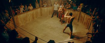 Movie still from “Triple Threat” (2019), directed by Jesse V. Johnson – A group of people watching two men fight in a boxing ring; Wide shot, High angle