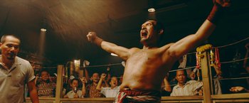 Movie still from “Triple Threat” (2019), directed by Jesse V. Johnson – A man in a boxing ring with his hands in the air; Medium shot, Low angle