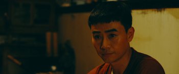 Movie still from “Triple Threat” (2019), directed by Jesse V. Johnson – A young man with short black hair is looking at the camera; Close Up shot, Over the shoulder angle