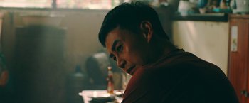 Movie still from “Triple Threat” (2019), directed by Jesse V. Johnson – A person sitting at a table; Close Up shot, Over the shoulder angle