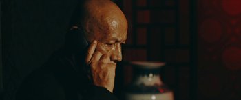 Movie still from “Triple Threat” (2019), directed by Jesse V. Johnson – A bald man is talking on a cell phone; Close Up shot, Over the shoulder angle