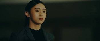 Movie still from “Triple Threat” (2019), directed by Jesse V. Johnson – A woman in a black jacket is looking at the camera; Close Up shot, Over the shoulder angle