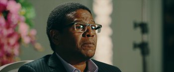 Movie still from “Triple Threat” (2019), directed by Jesse V. Johnson – An older man wearing glasses and a suit; Close Up shot, Over the shoulder angle