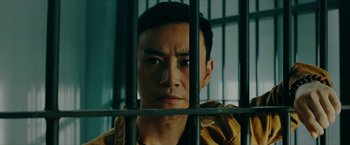 Movie still from “Triple Threat” (2019), directed by Jesse V. Johnson – A man standing behind bars in front of a window; Close Up shot, Low angle