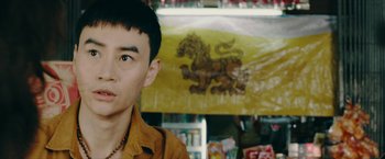 Movie still from “Triple Threat” (2019), directed by Jesse V. Johnson – A man standing in front of a store with a flag in the background; Close Up shot, Over the shoulder angle