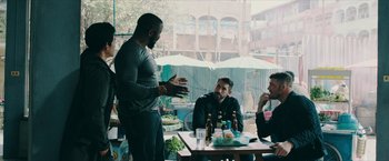 Movie still from “Triple Threat” (2019), directed by Jesse V. Johnson – A group of men sitting at a table with drinks; Medium shot, Over the shoulder angle