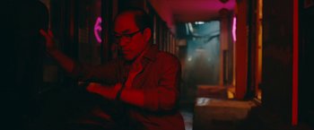 Movie still from “Triple Threat” (2019), directed by Jesse V. Johnson – A man wearing glasses is looking at his watch; Medium shot, Over the shoulder angle