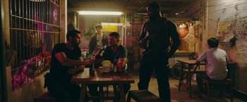 Movie still from “Triple Threat” (2019), directed by Jesse V. Johnson – A group of men sitting at a table with drinks; Medium shot, Over the shoulder angle