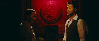 Movie still from “Triple Threat” (2019), directed by Jesse V. Johnson – Two men standing in front of a red wall; Medium shot, Over the shoulder angle