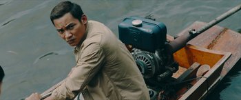 Movie still from “Triple Threat” (2019), directed by Jesse V. Johnson – A man sitting on the back of a motor boat; Medium shot, High angle