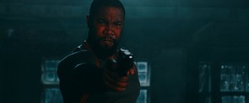 Movie still from “Triple Threat” (2019), directed by Jesse V. Johnson – A man holding a gun in a dark room; Close Up shot, Low angle