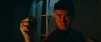 Movie still from “Triple Threat” (2019), directed by Jesse V. Johnson – A young man with a serious look on his face in front of a window; Close Up shot, Low angle