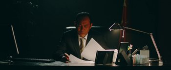 Movie still from “Triple Threat” (2019), directed by Jesse V. Johnson – A man sitting at a desk in front of a computer; Medium shot, Low angle